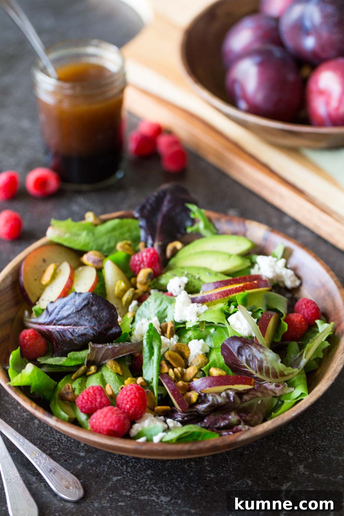 Summer Fruit Salad with Goat Cheese & Pistachios for Entertaining 3 Summer Fruited Salad with Goat Cheese and Pistachios in a wood bowl, with a jar of homemade balsamic vinaigrette in the background along with a bowl of whole plums.