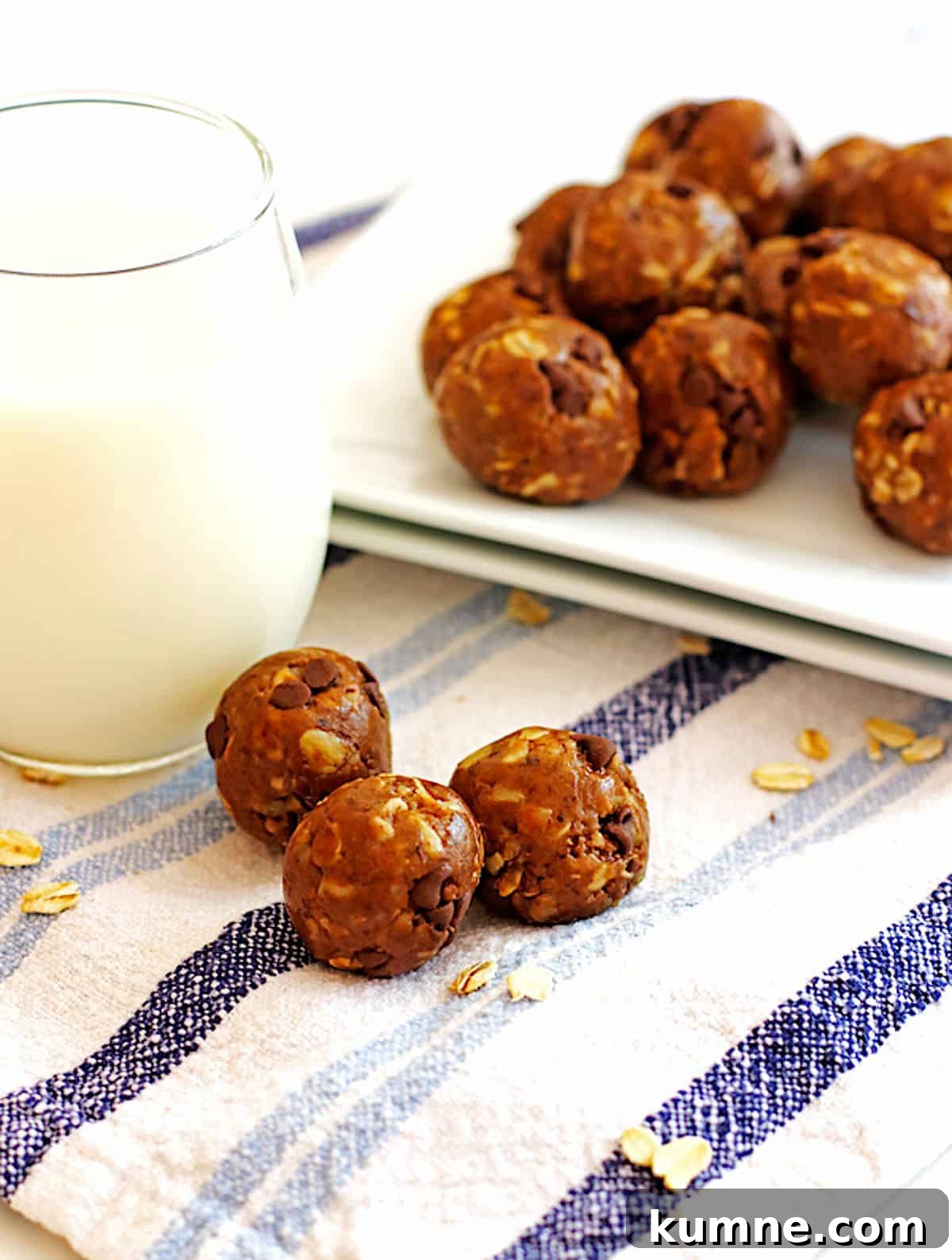 No-Bake Peanut Butter Energy Balls Recipe for Quick Snacks 2 A plate of peanut butter energy bites on a white plate being picked up by a hand with a glass of milk and three in the front.