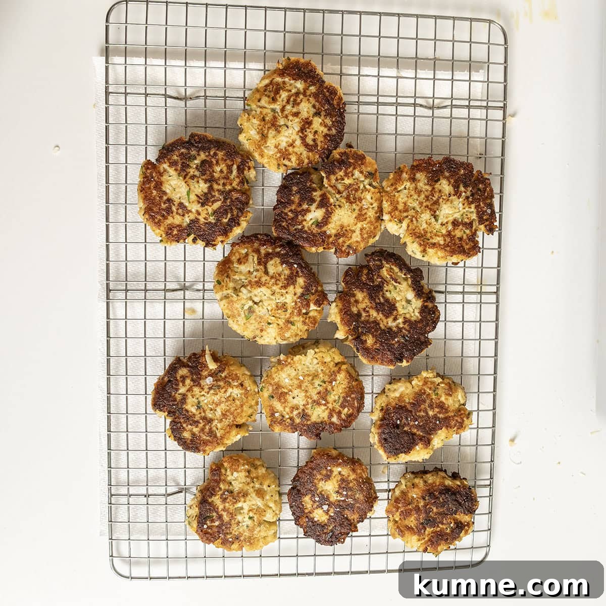 Fried cauliflower cakes on a cooling rack, sprinkled with salt.