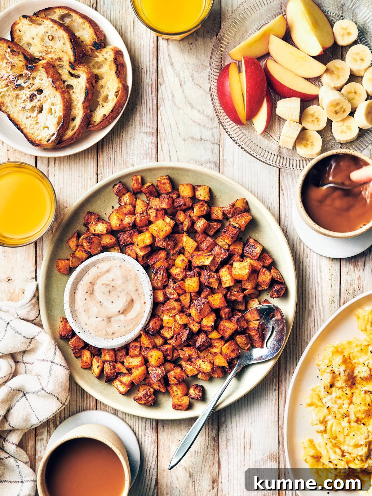 A plate of air fryer breakfast potatoes with dip on the breakfast table with juice, coffee, fruit, eggs, toast.
