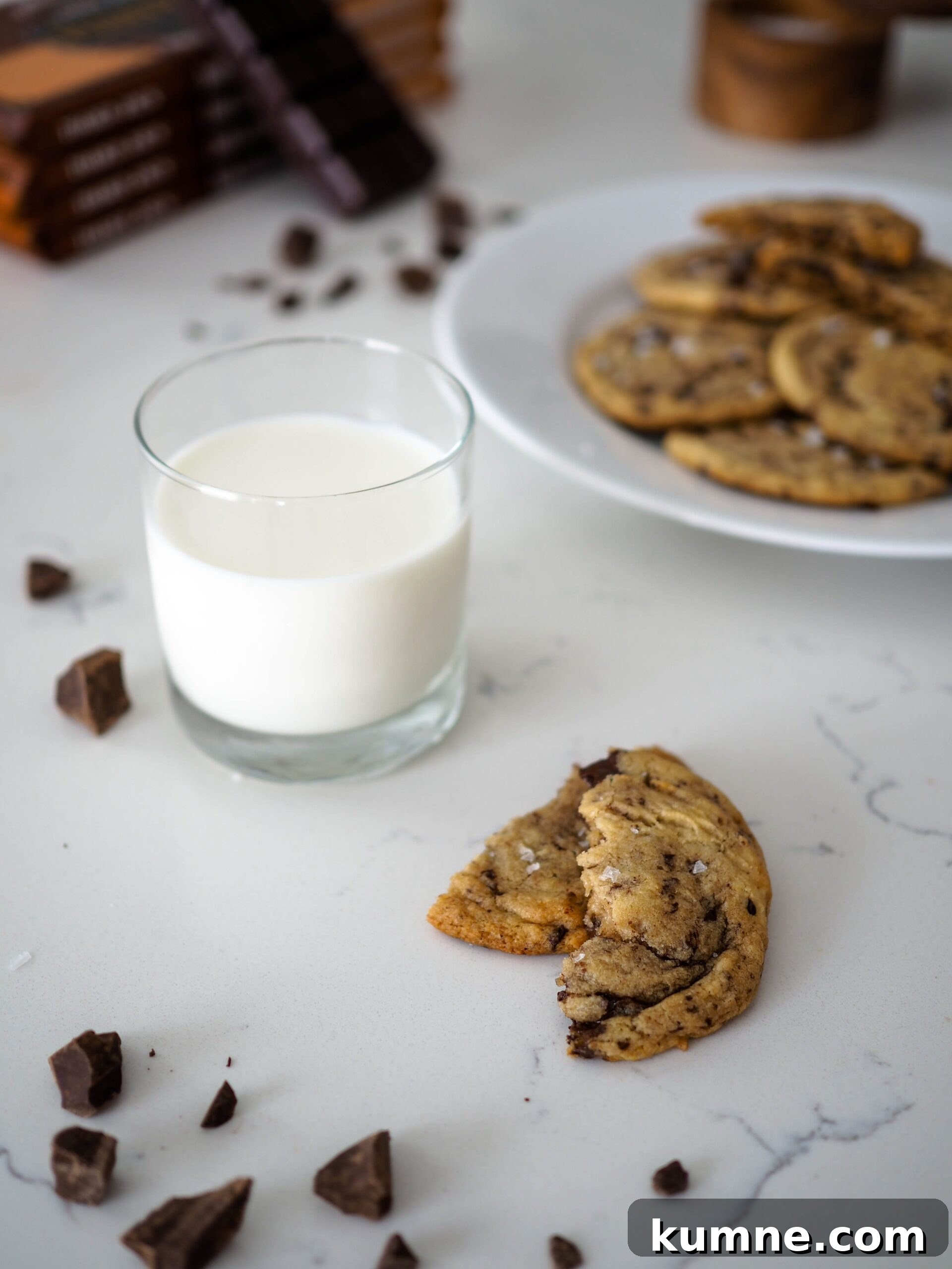 Decadent Dark Chocolate Chunk Cookie Recipe 2 A glass of milk beside two halves of a chocolate chip cookie.