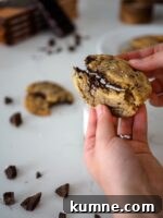 Decadent Dark Chocolate Chunk Cookie Recipe 8 A dark chocolate chip cookie is broken in half by two hands.