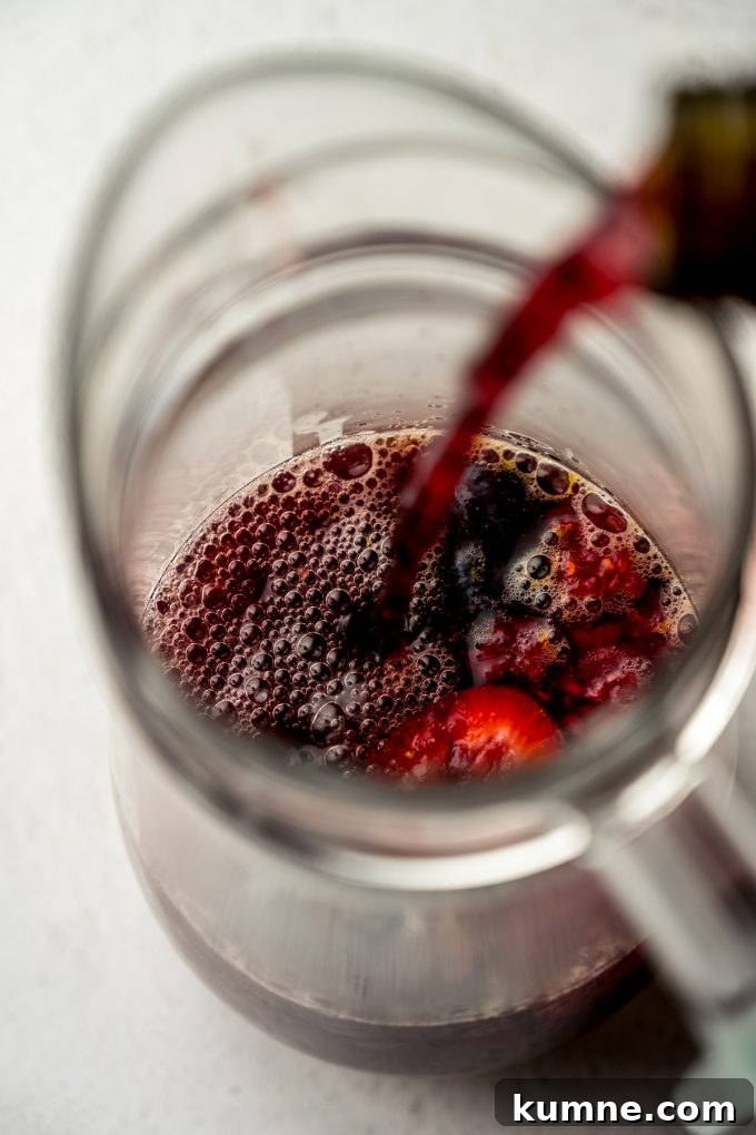 Berry Sangria and Refreshing Non-Alcoholic Berry Mocktail 12 Aerial photo of someone pouring nonalcoholic wine into berry sangria in a pitcher.