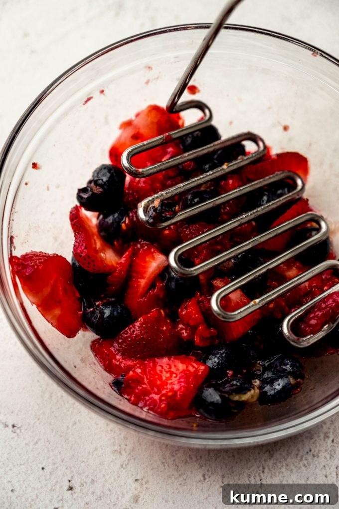 Berry Sangria and Refreshing Non-Alcoholic Berry Mocktail 7 A bowl of blueberries, strawberries, and raspberries getting macerated with a potato masher.