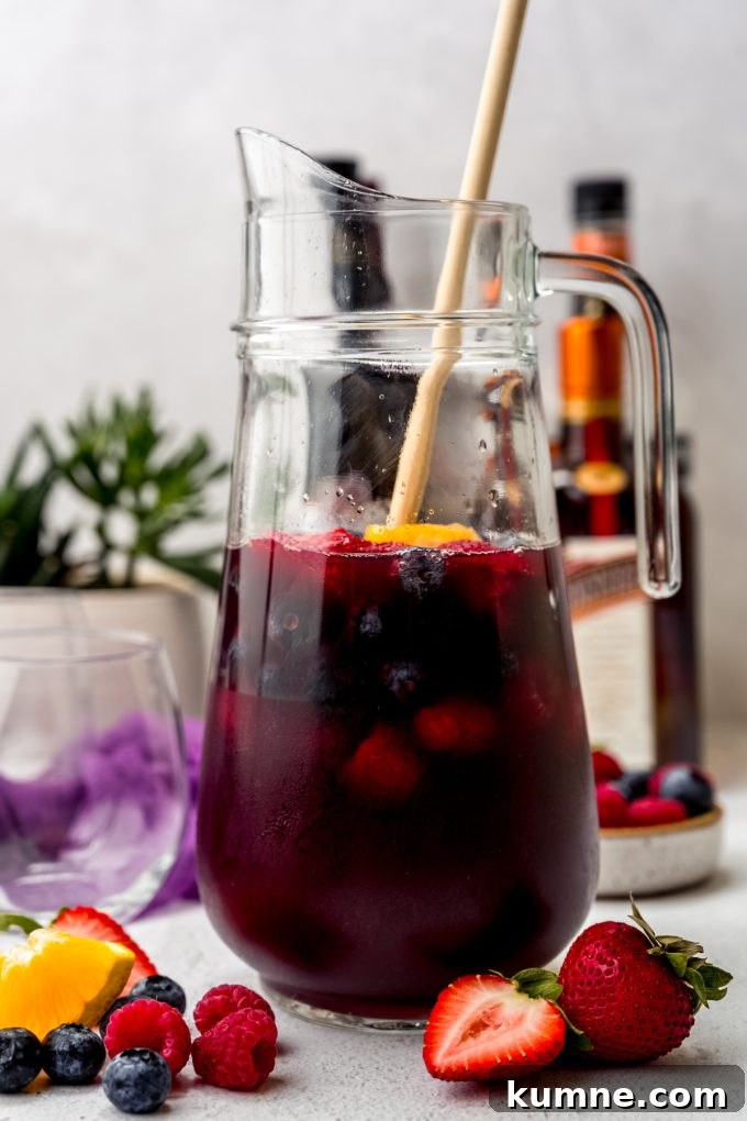 Berry Sangria and Refreshing Non-Alcoholic Berry Mocktail 9 A glass pitcher of berry sangria with a wooden spoon in it.