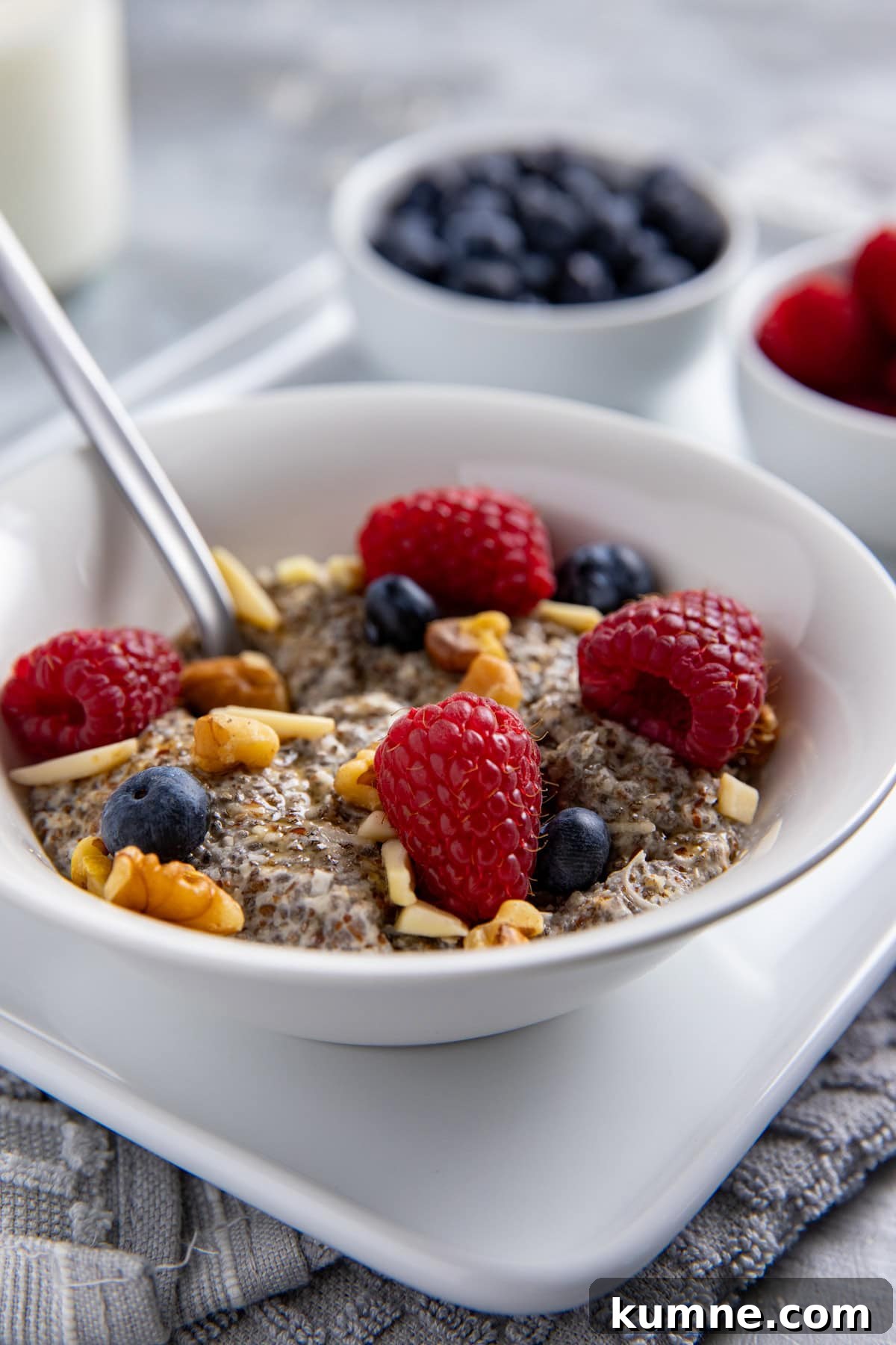 Creamy Chia Seed Breakfast Bowl with Fruit and Granola 2 Warm Chia Breakfast Bowl with Berries & Nuts in a white bowl on a white platter with a spoon inside the bowl.