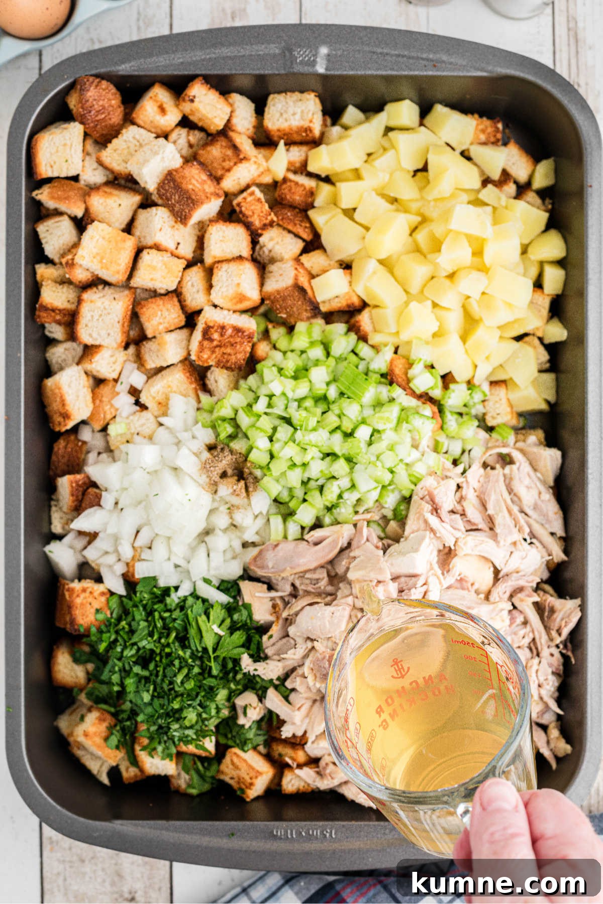 Chicken broth being poured into a large roaster with other ingredients.