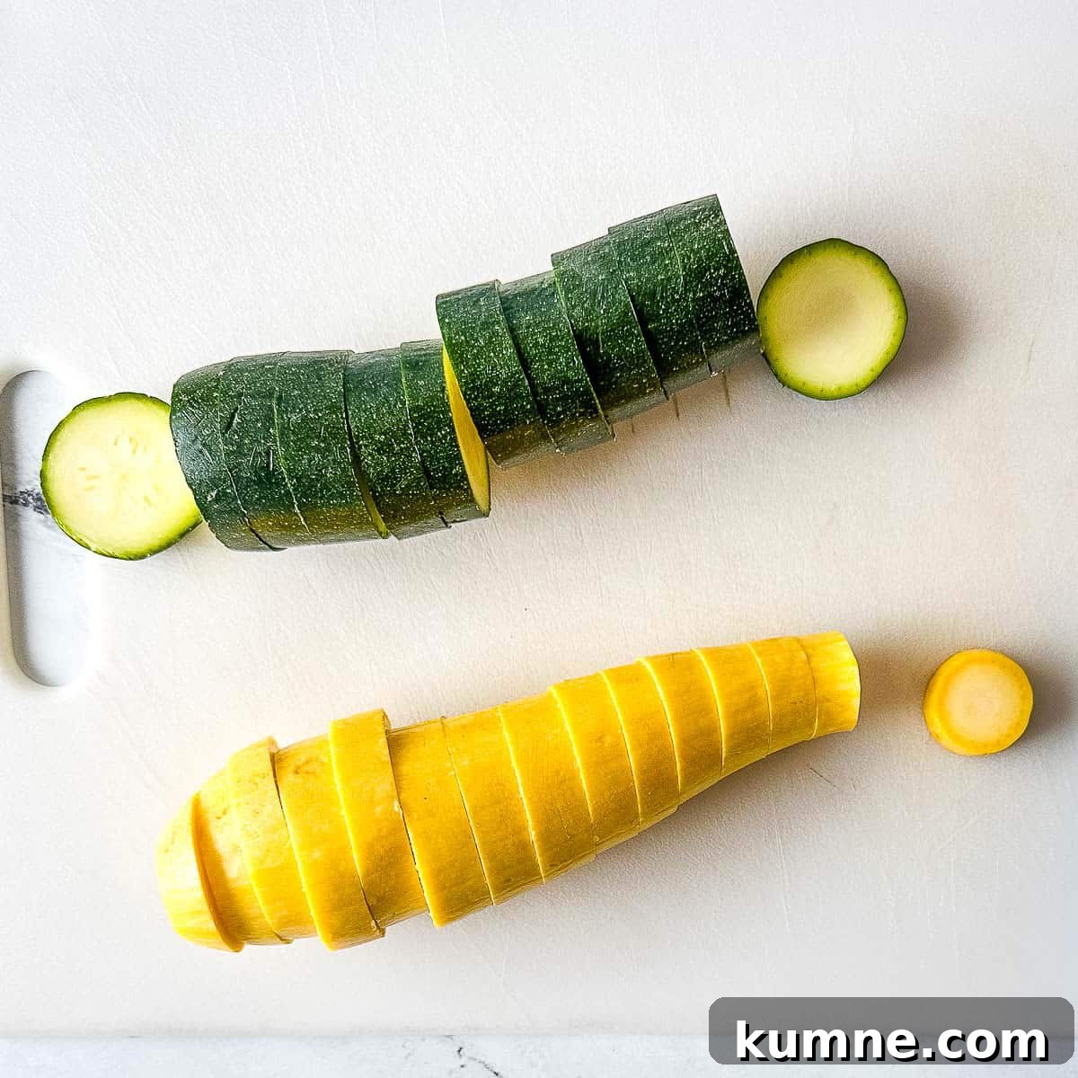 Sliced zucchini and yellow summer squash sit on a white cutting board.