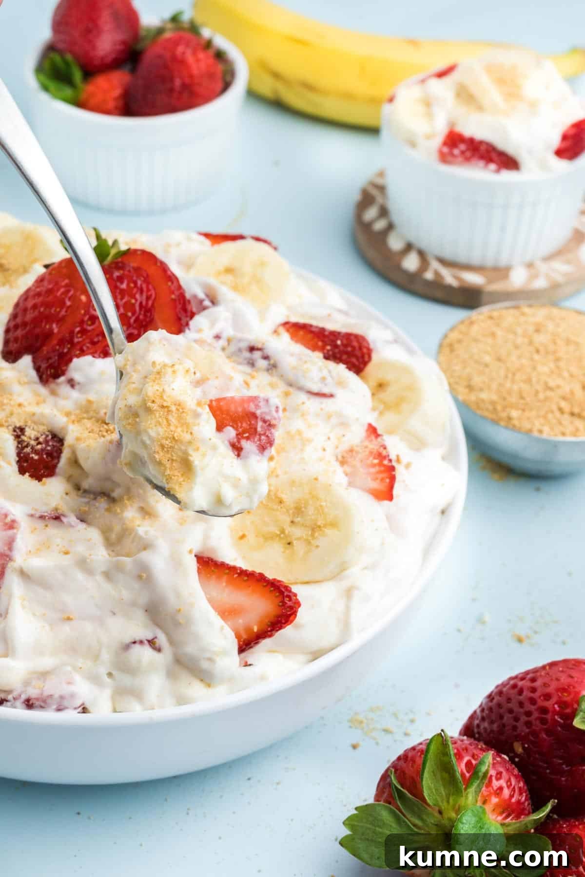 A bowl of strawberry banana cheesecake salad on the table with a spoon taking a bite.