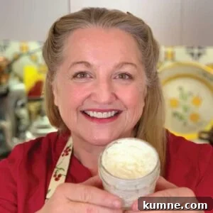 Mary holding up a jar of homemade foot cream while standing in her kitchen.