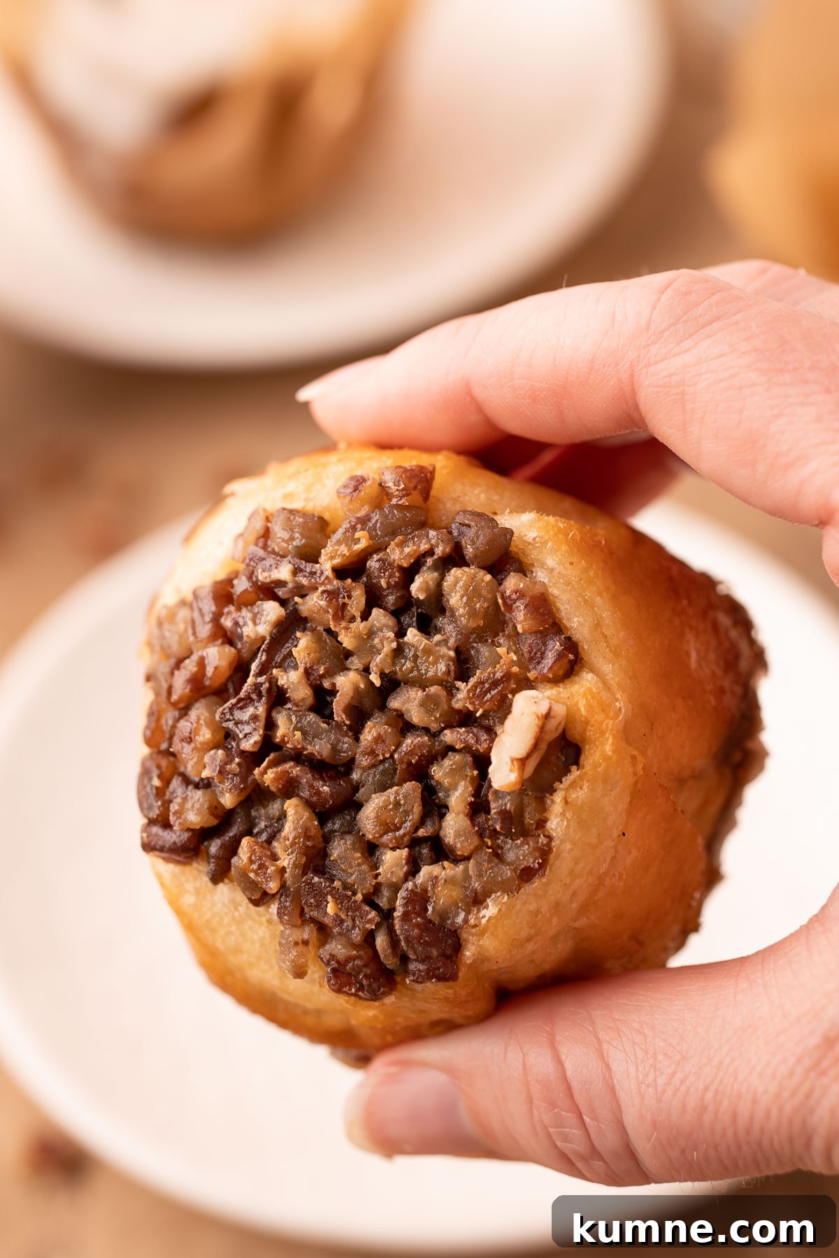 A woman's hand holding a pecan roll muffin showing the bottom.