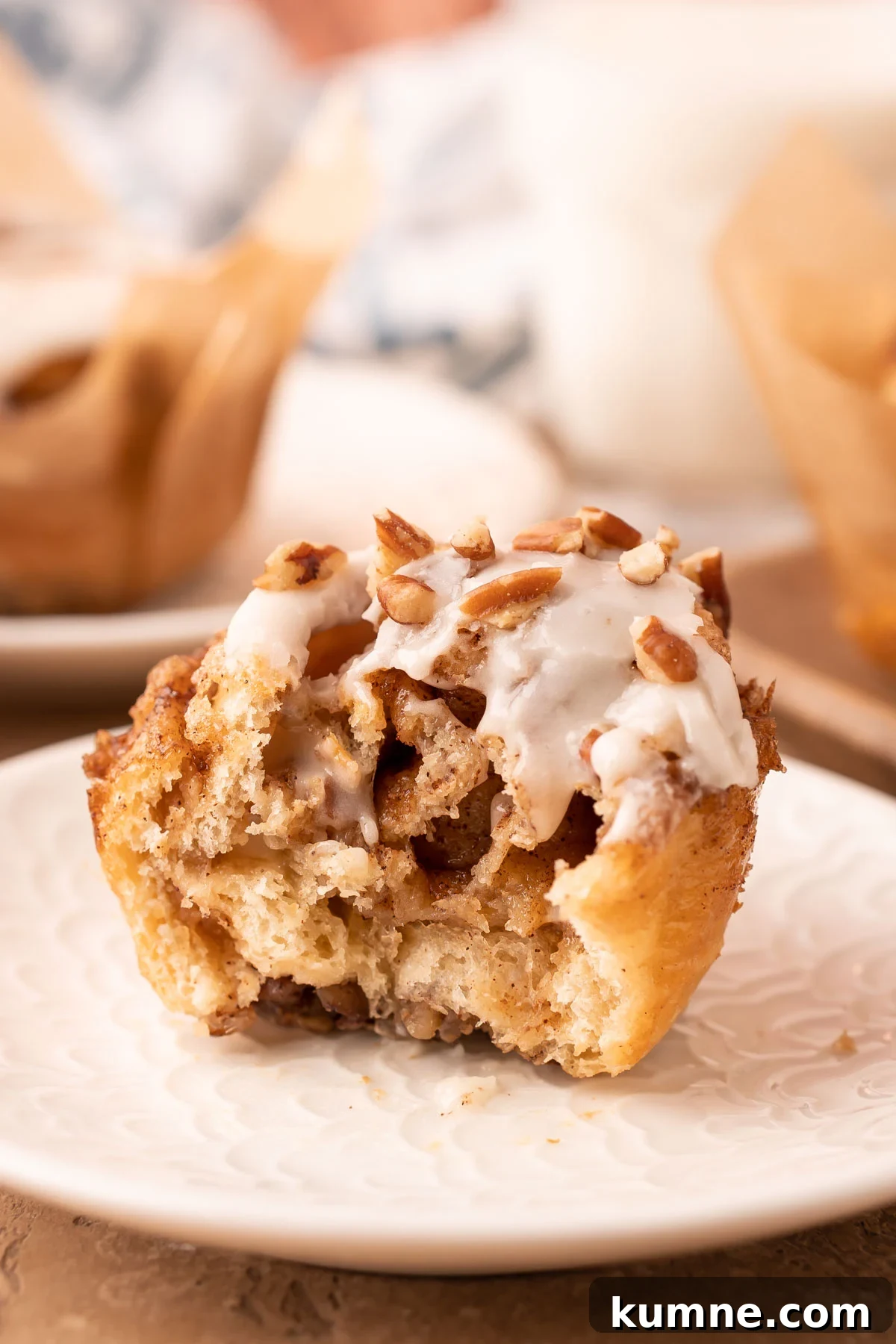 A crescent roll cinnamon pecan roll muffin on a white plate with a bite missing.