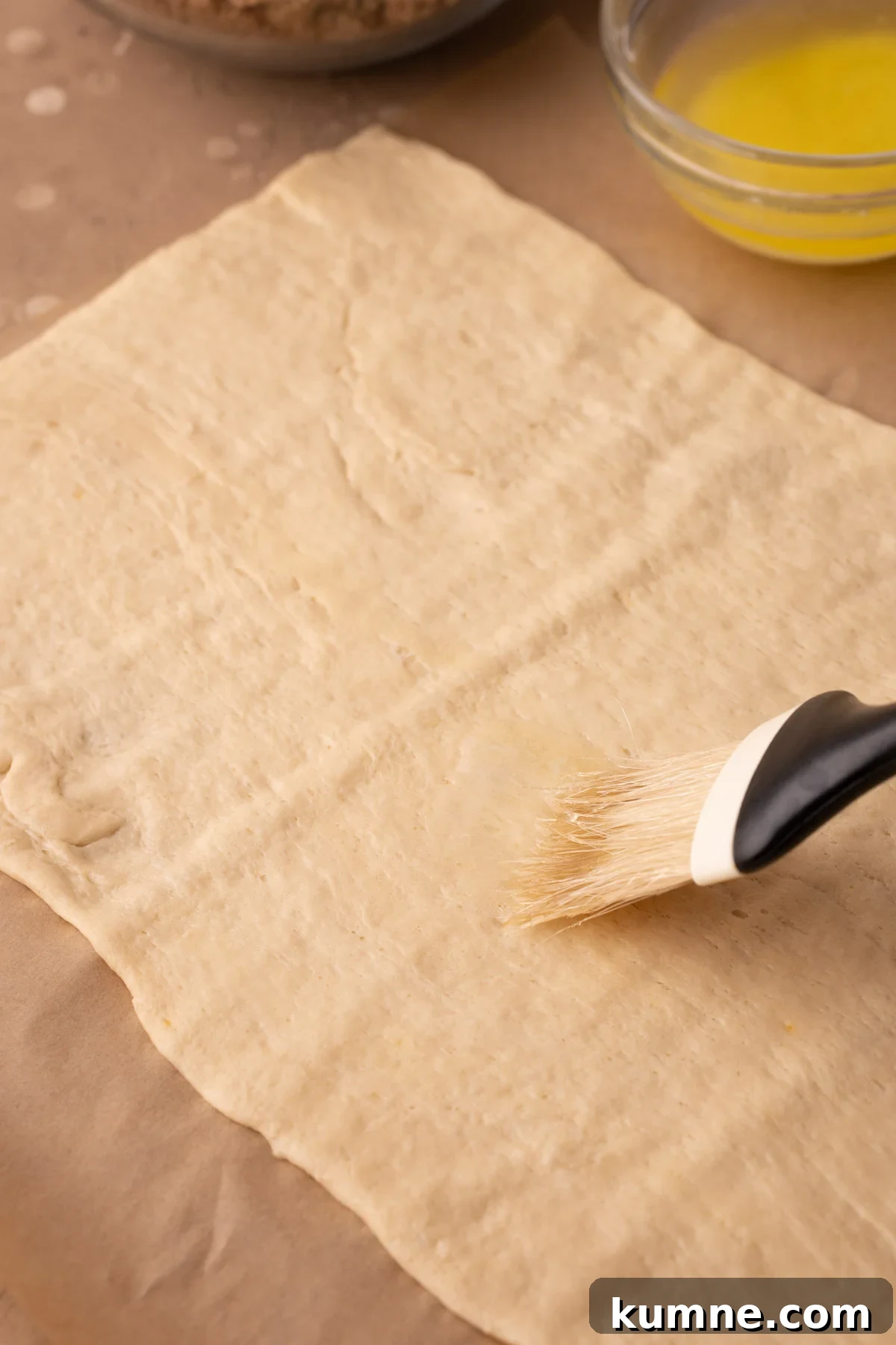 A pastry brush brushing a crescent roll dough sheet with melted butter.