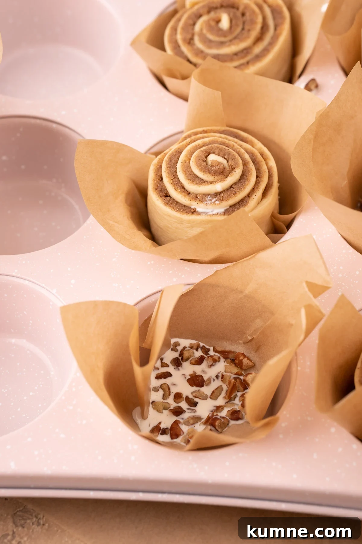 A muffin tin being filled with liners to make cinnamon rolls.