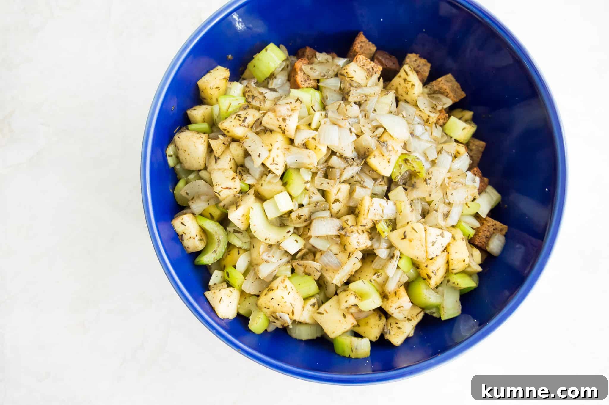 Gluten-Free Paleo Stuffing Made with Paleo Bread 5 A bowl with dried bread cubes in it that are topped with cooked onions, apples and celery.