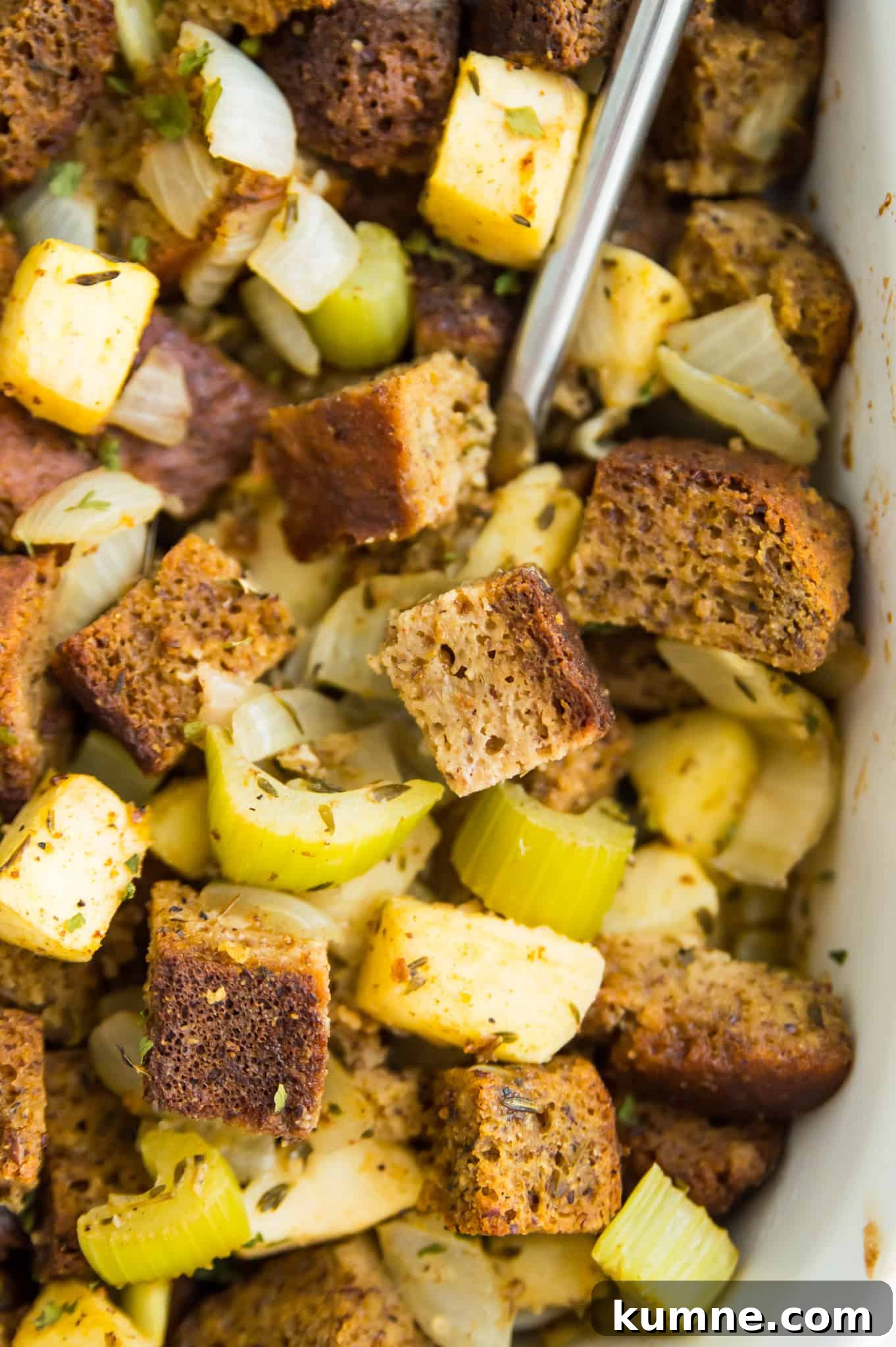 Gluten-Free Paleo Stuffing Made with Paleo Bread 9 A casserole dish filled with stuffing made with bread cubes, apples and celery with a serving spoon in it.