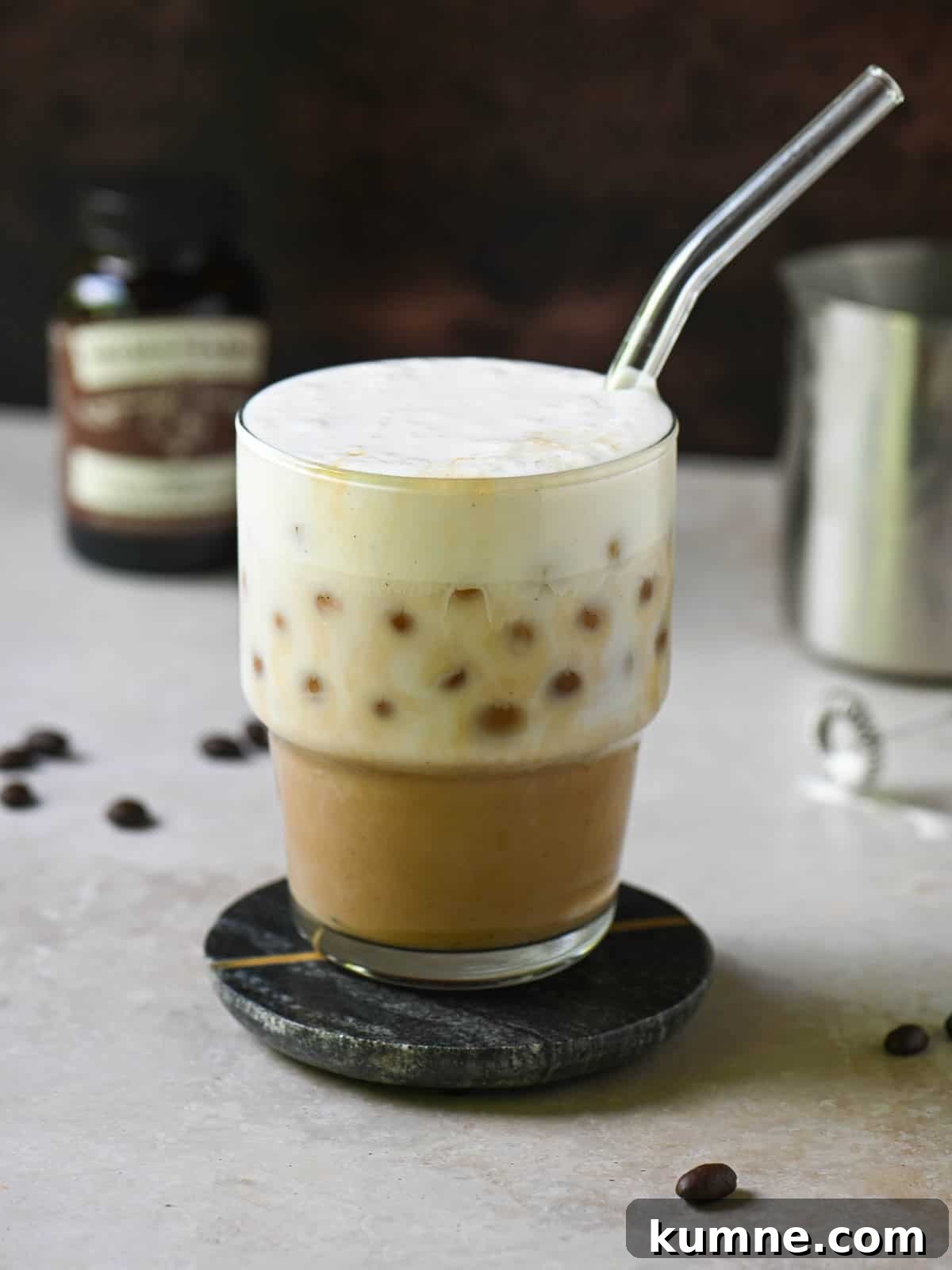 Iced Vanilla Bean Latte Recipe Using Real Vanilla Extract 2 Eye-level view of a vanilla bean latte on a brown surface.