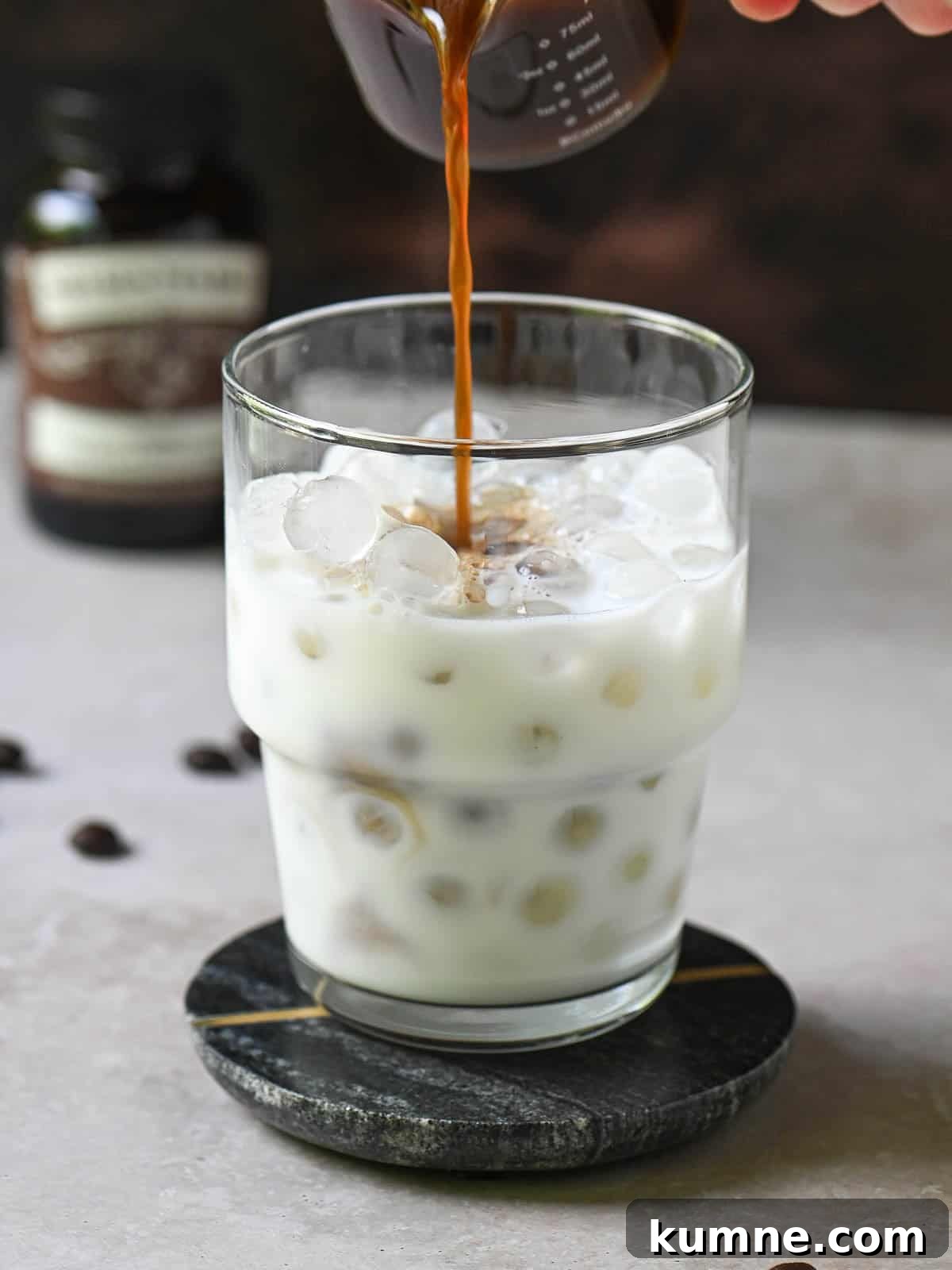 Iced Vanilla Bean Latte Recipe Using Real Vanilla Extract 6 Coffee is being poured into a clear glass with milk and ice.
