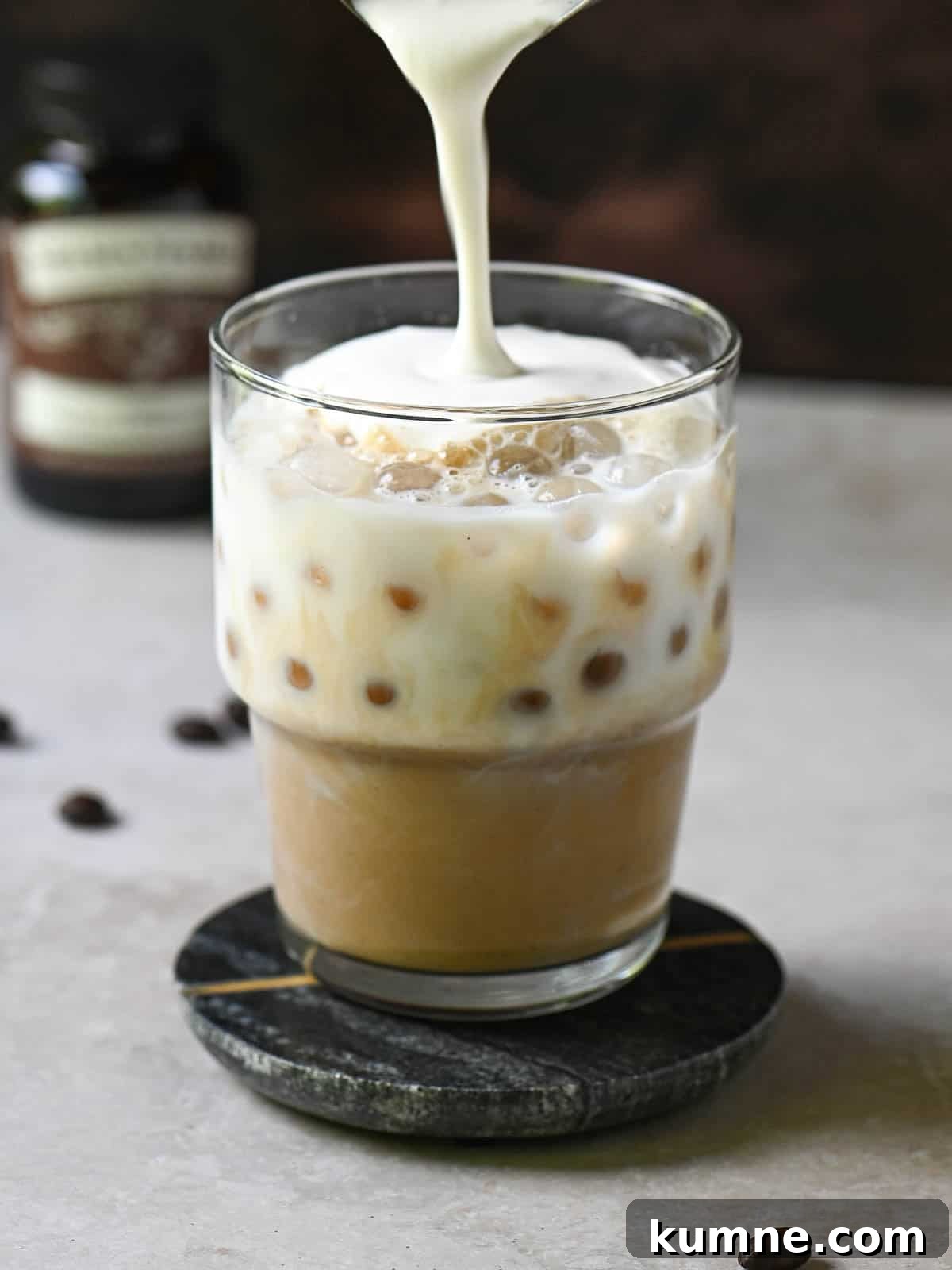 Iced Vanilla Bean Latte Recipe Using Real Vanilla Extract 7 Cold foam is being poured into a clear glass with coffee and milk.