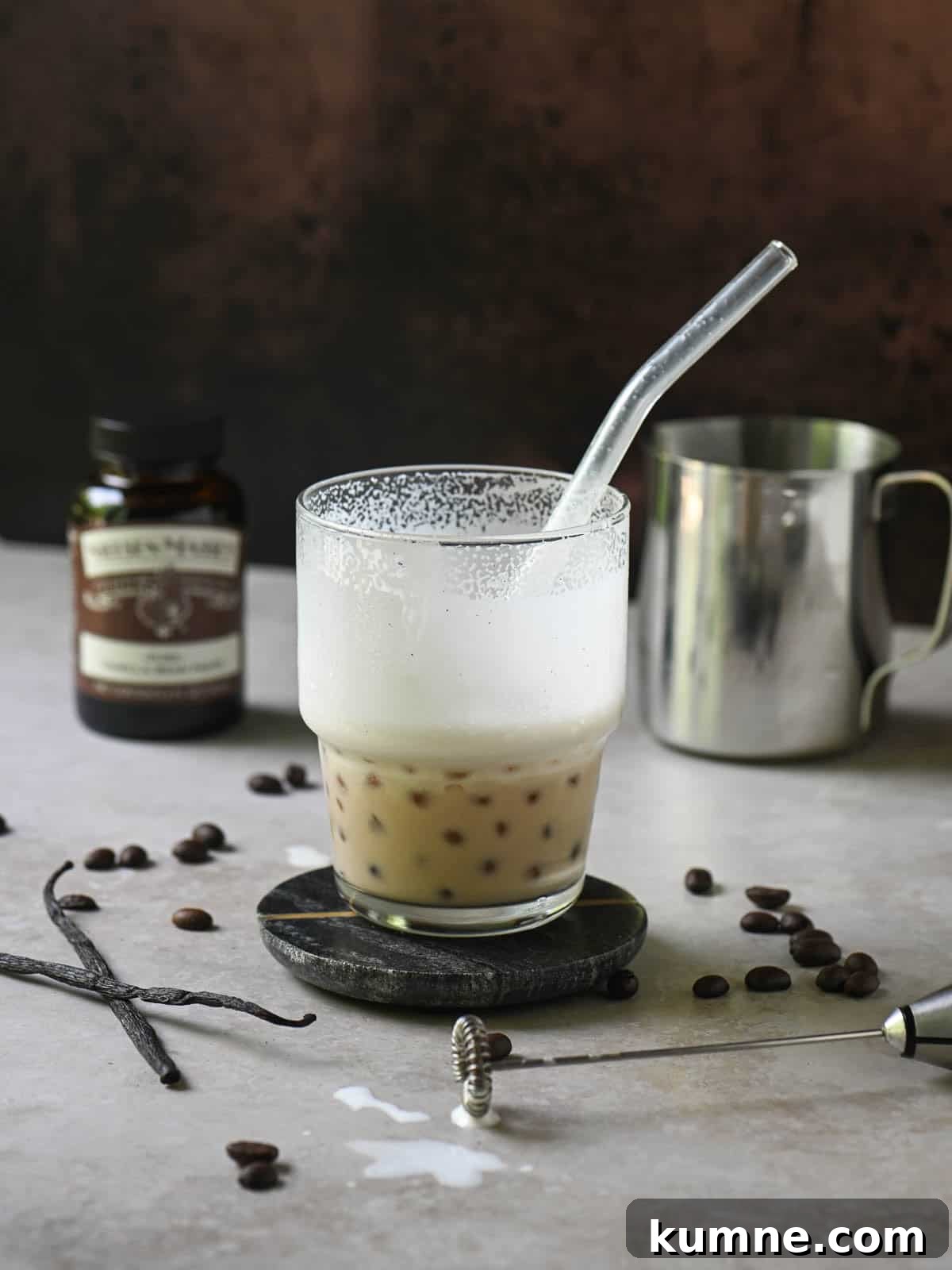 Iced Vanilla Bean Latte Recipe Using Real Vanilla Extract 9 Eye-level view of a half-empty coffee latte in a clear cup on a beige surface.