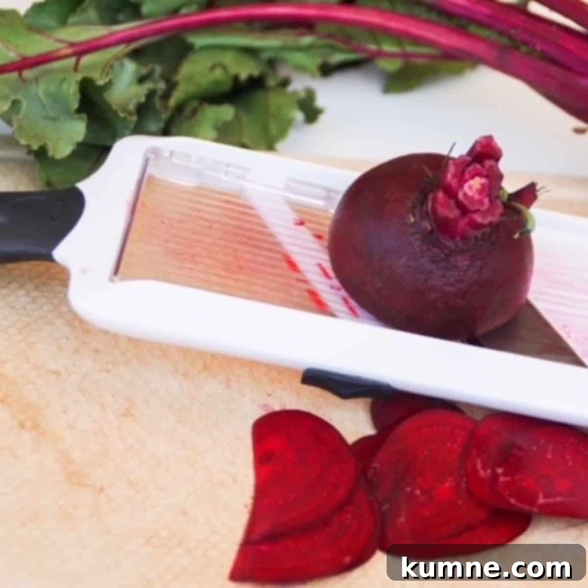 Beet being sliced with a mandolin slicer over a cutting board.