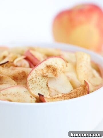 Air fried apple slices in a white bowl with an apple in the background.