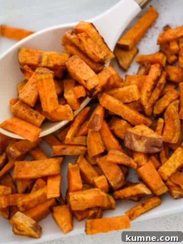Chunks of roasted sweet potatoes on a white plate with a white and gold serving spoon.