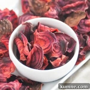 Beet chips in a white bowl on a white platter with more beet chips.