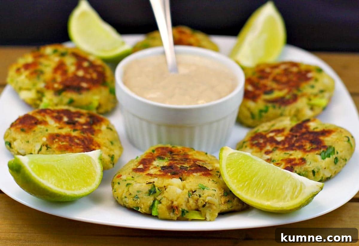 Pan-fried salmon patties on white plate, with dip in the middle and lime wedges