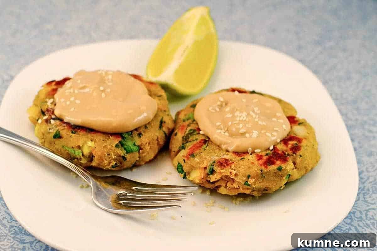 2 Pan-fried Salmon Patties on a white plate with creamy sauce on top and a fork and lime wedge on the plate. 