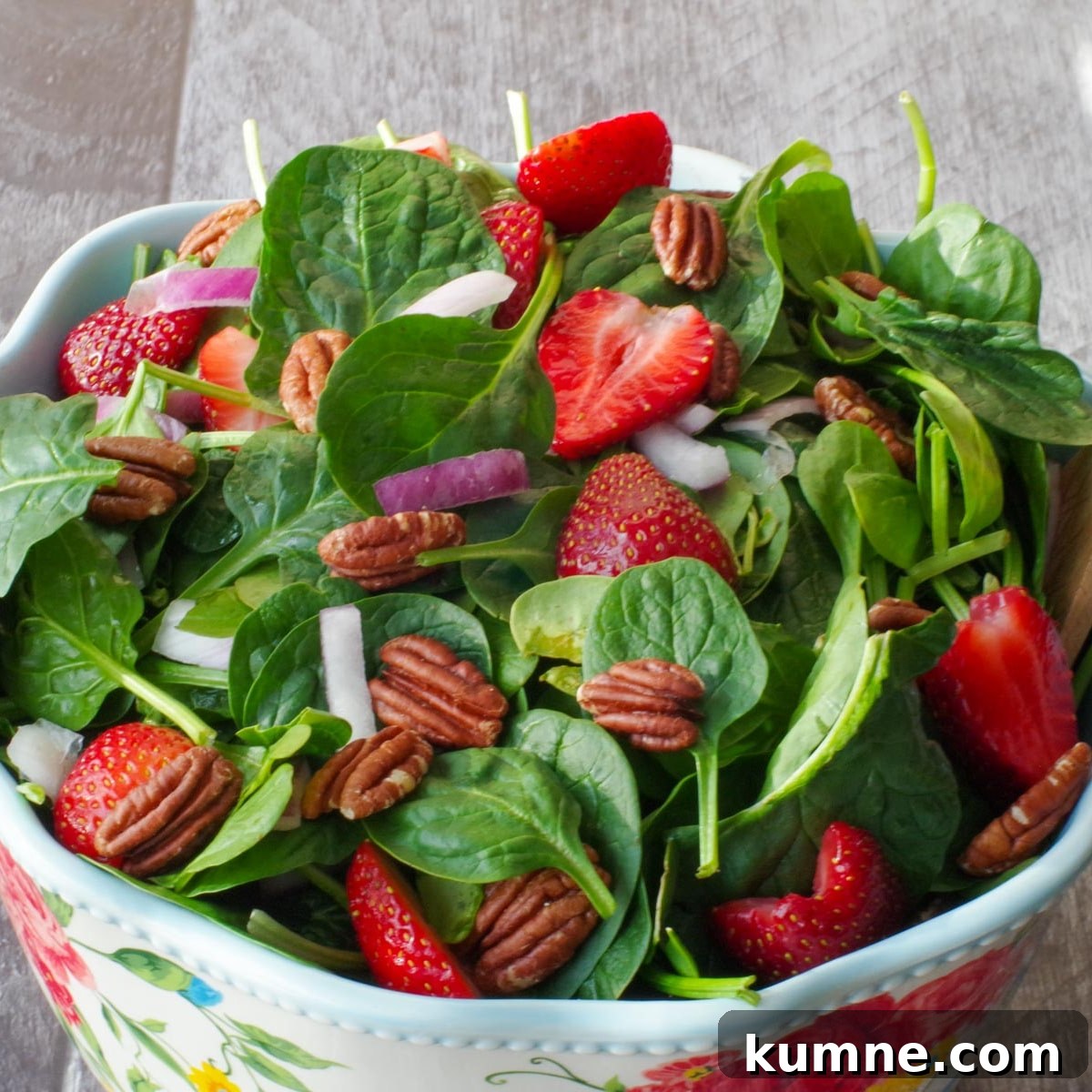 strawberry spinach pecan salad in a large bowl with flower print and wooden utensils