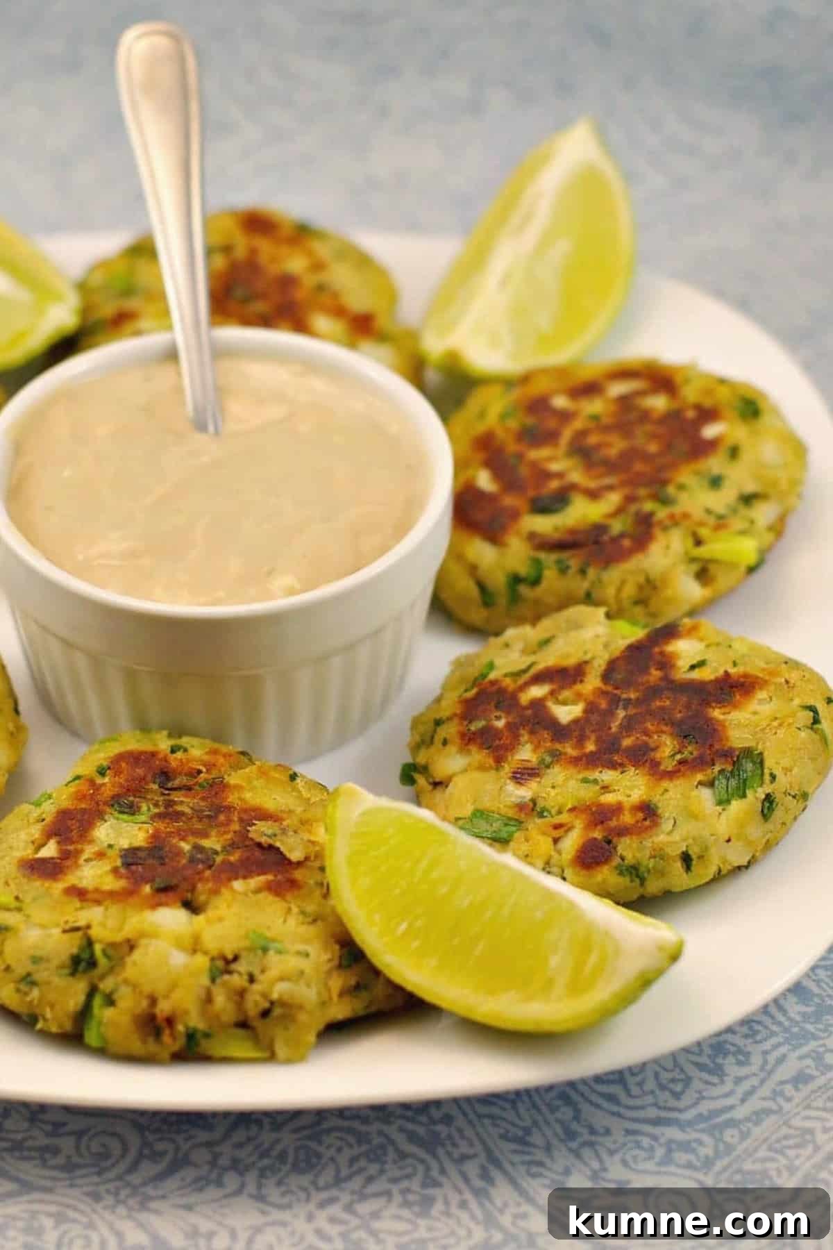 Salmon patties on a white plate, with sauce in the middle and lime wedges.