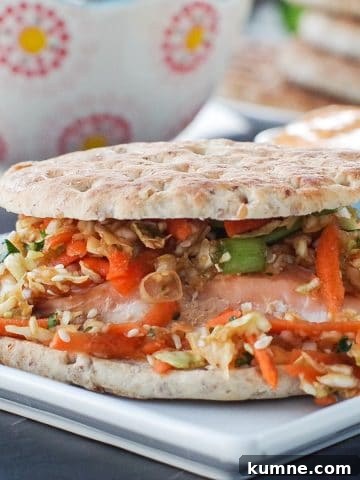 salmon burger on white plate with coleslaw, buns on a plate and sriracha mayo in background
