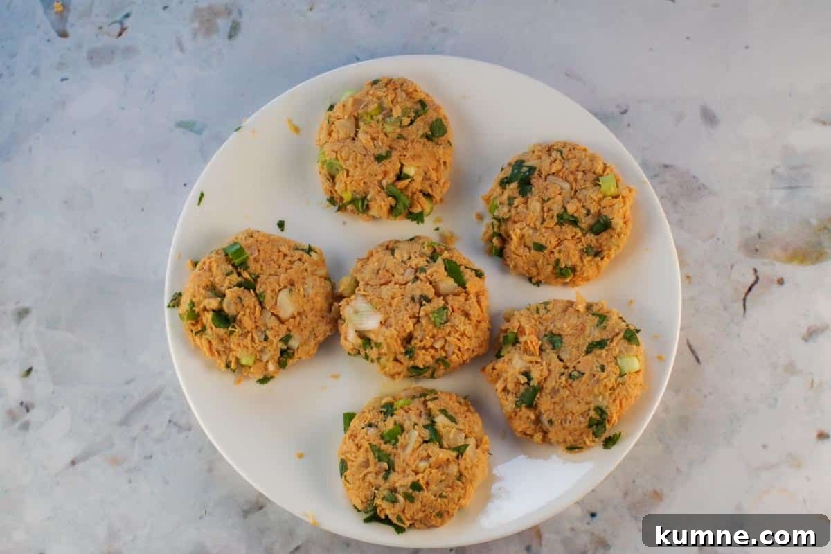 6 uncooked salmon patties on a white plate.