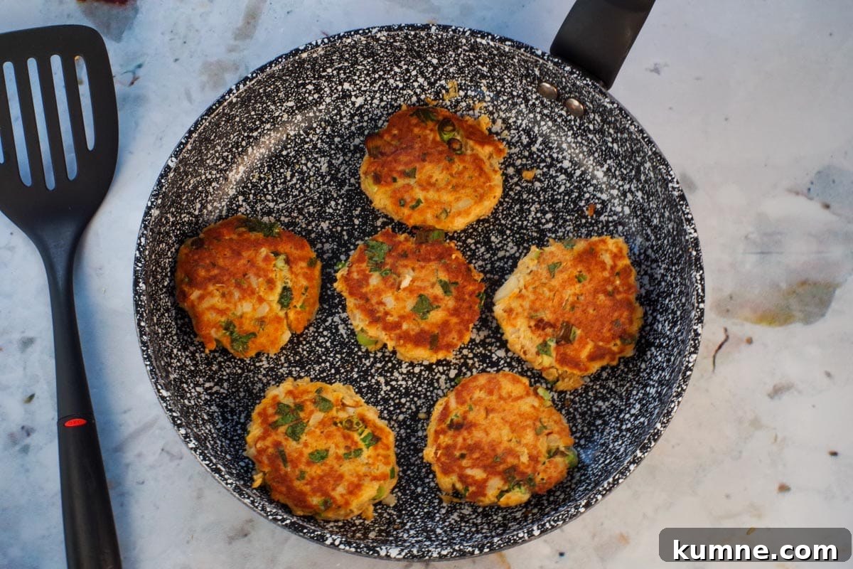 6 salmon patties in frying pan cooked on one side.