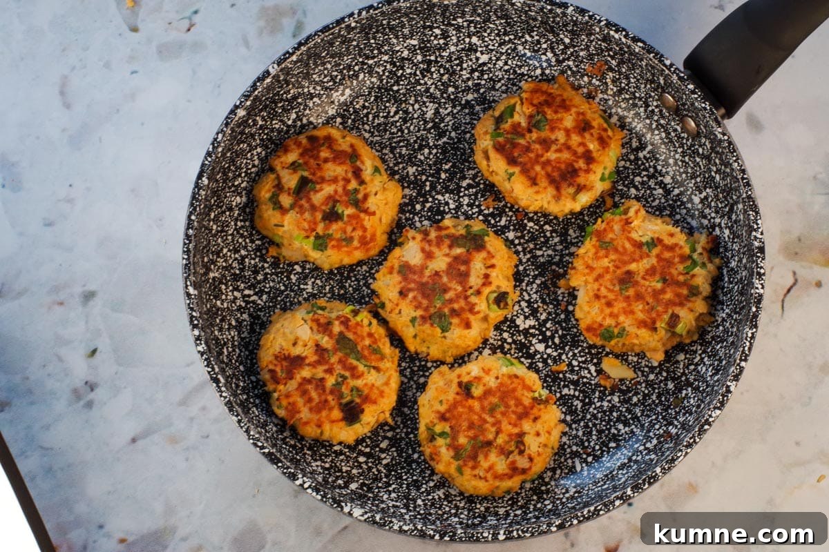 Salmon patties cooked on both sides in frying pan.