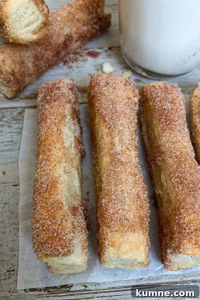 Crispy Oven-Baked Churros Recipe you Can Make at Home 5 baked churros on a piece of parchment paper with milk for serving