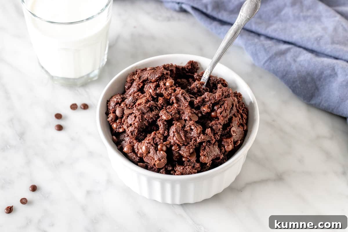 Bowl of edible chocolate brownie batter with a spoon in it.