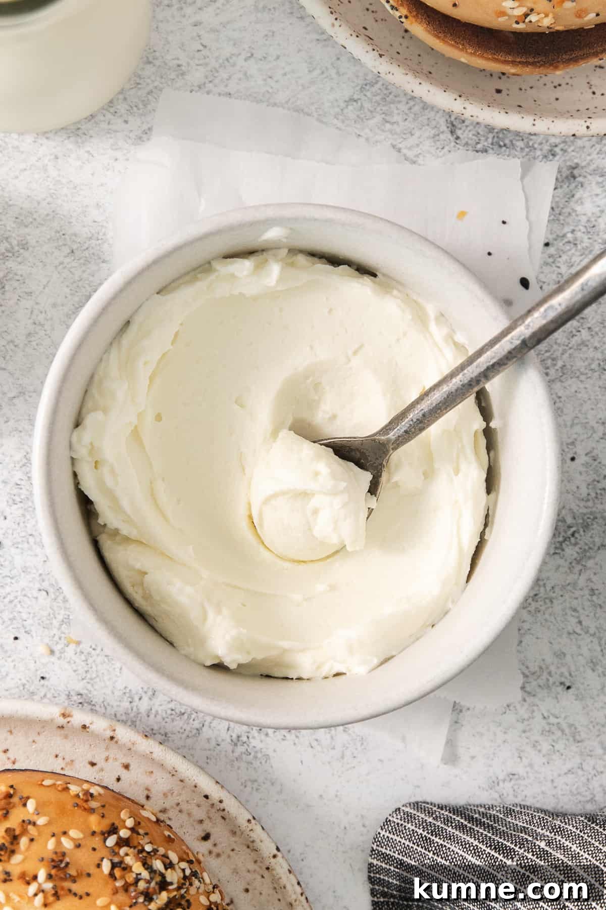a bowl of cream cheese with a spoon next to a baguette.