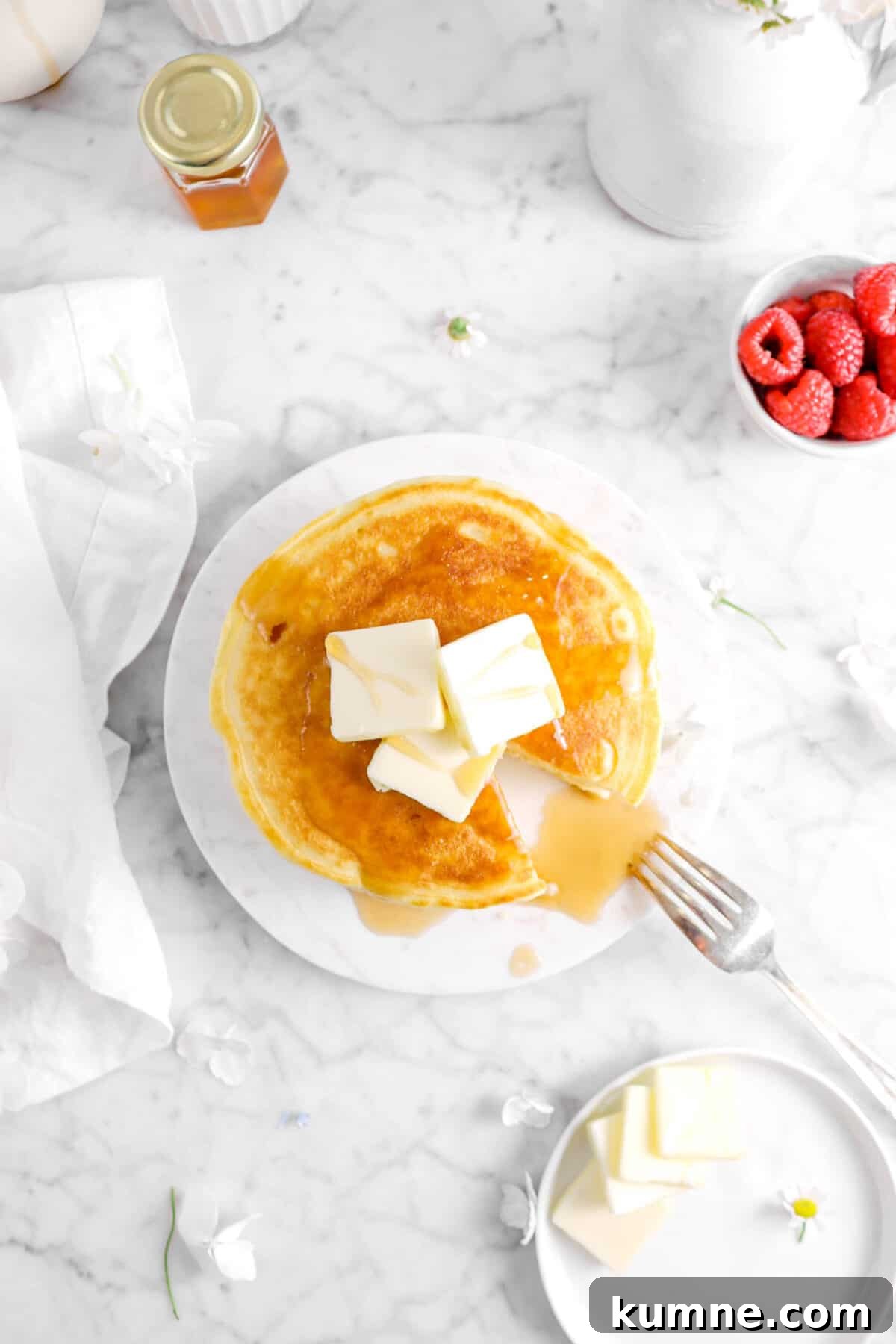 Fluffy Homemade Buttermilk Pancakes Recipe for Perfect Mornings 9 overhead shot of buttermilk pancakes with a slice taken out of them, a bowl of raspberries, and butter