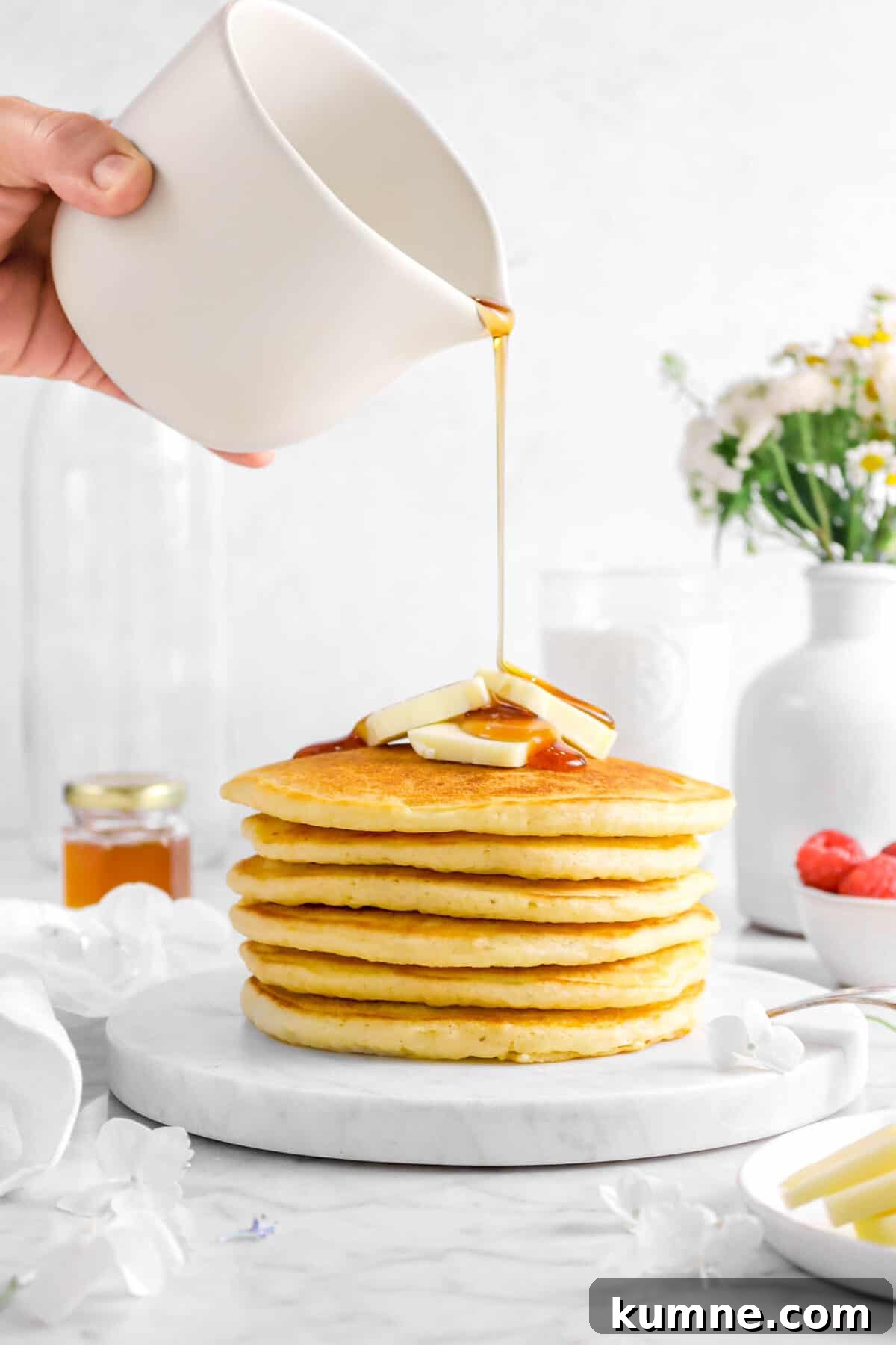 Fluffy Homemade Buttermilk Pancakes Recipe for Perfect Mornings 12 syrup being poured onto six stacked pancakes with flowers