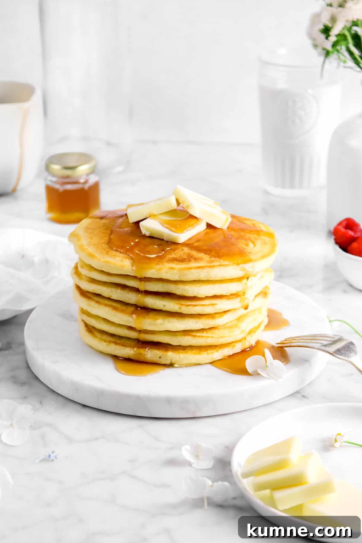 Fluffy Homemade Buttermilk Pancakes Recipe for Perfect Mornings 3 stacked buttermilk pancakes on marble plate with butter, syrup, and flowers