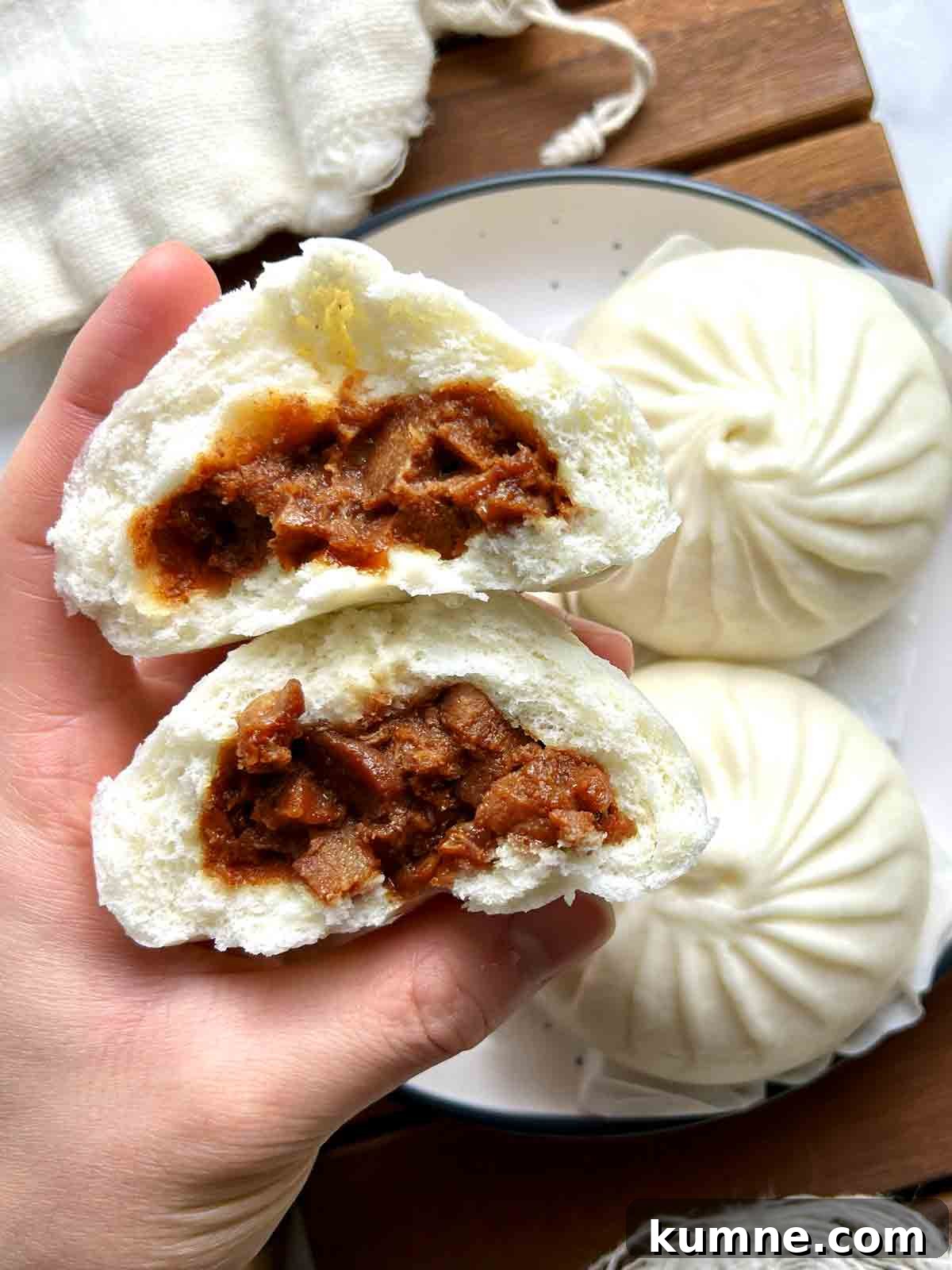 13 Steamed Bun Recipes You Need to Try Tonight 3 hand holding steamed bbq pork bun cut in half to show the filling.