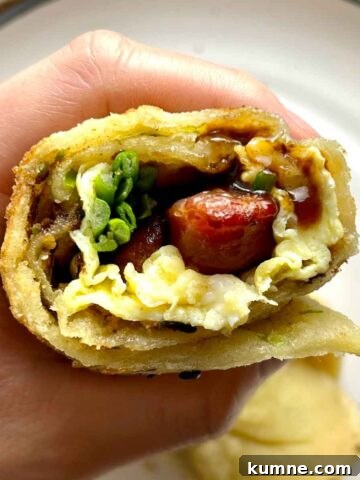 hand holding Chinese pancake filled with egg, Chinese sausage, sauce, and greens.