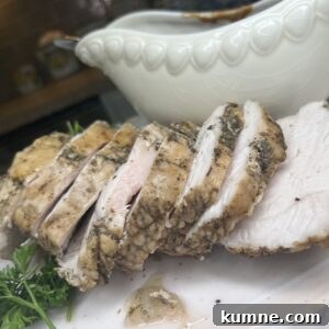 Sliced roasted pork tenderloin and turkey breast on a white plate, garnished with fresh herbs, with a white gravy boat in the background.