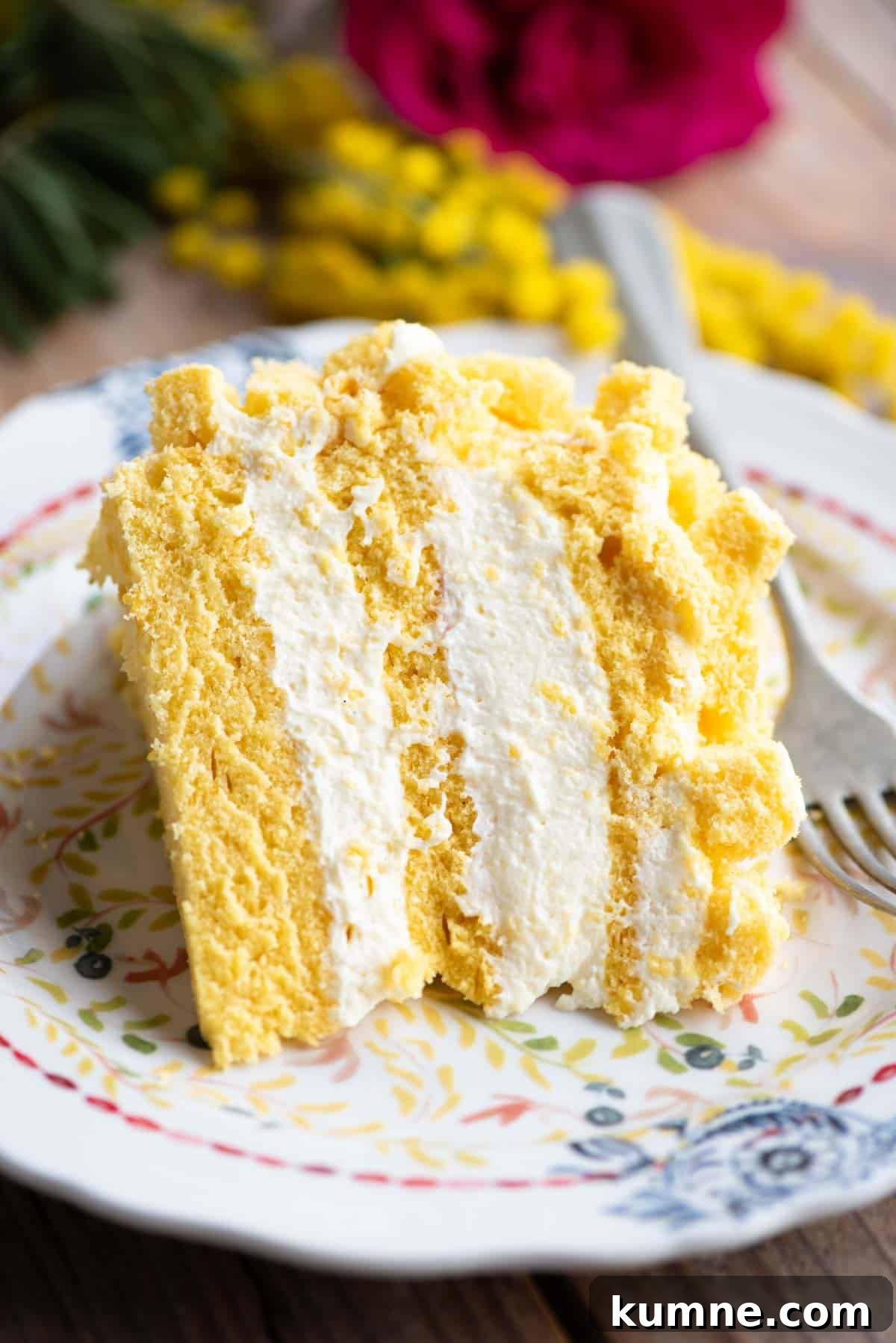 A slice of mimosa cake with three layers and filled with cream on a small plate.