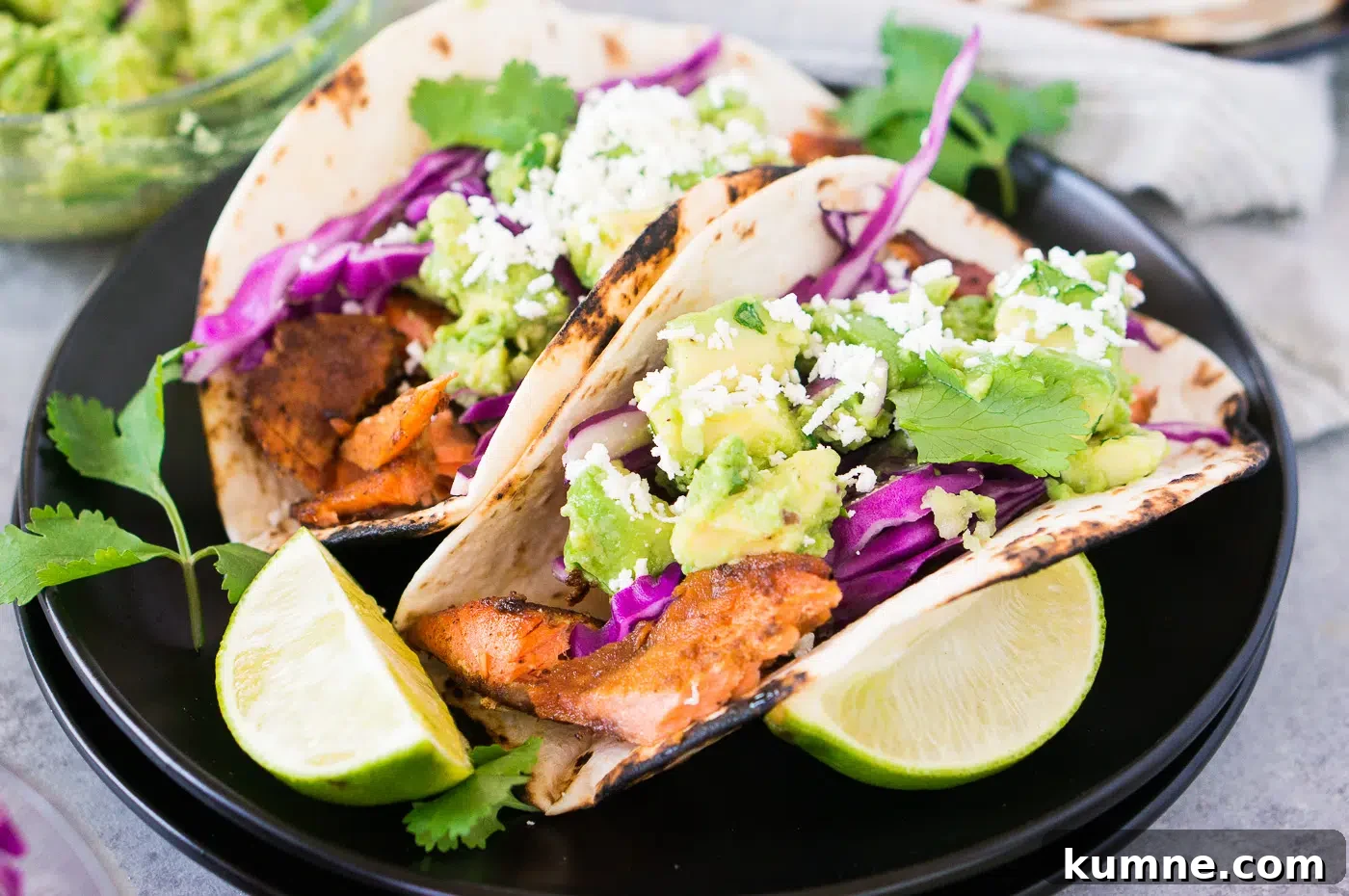Citrus-Glazed Salmon Tacos with Avocado Slaw 3 close up of salmon tacos with avocado salsa on black plates