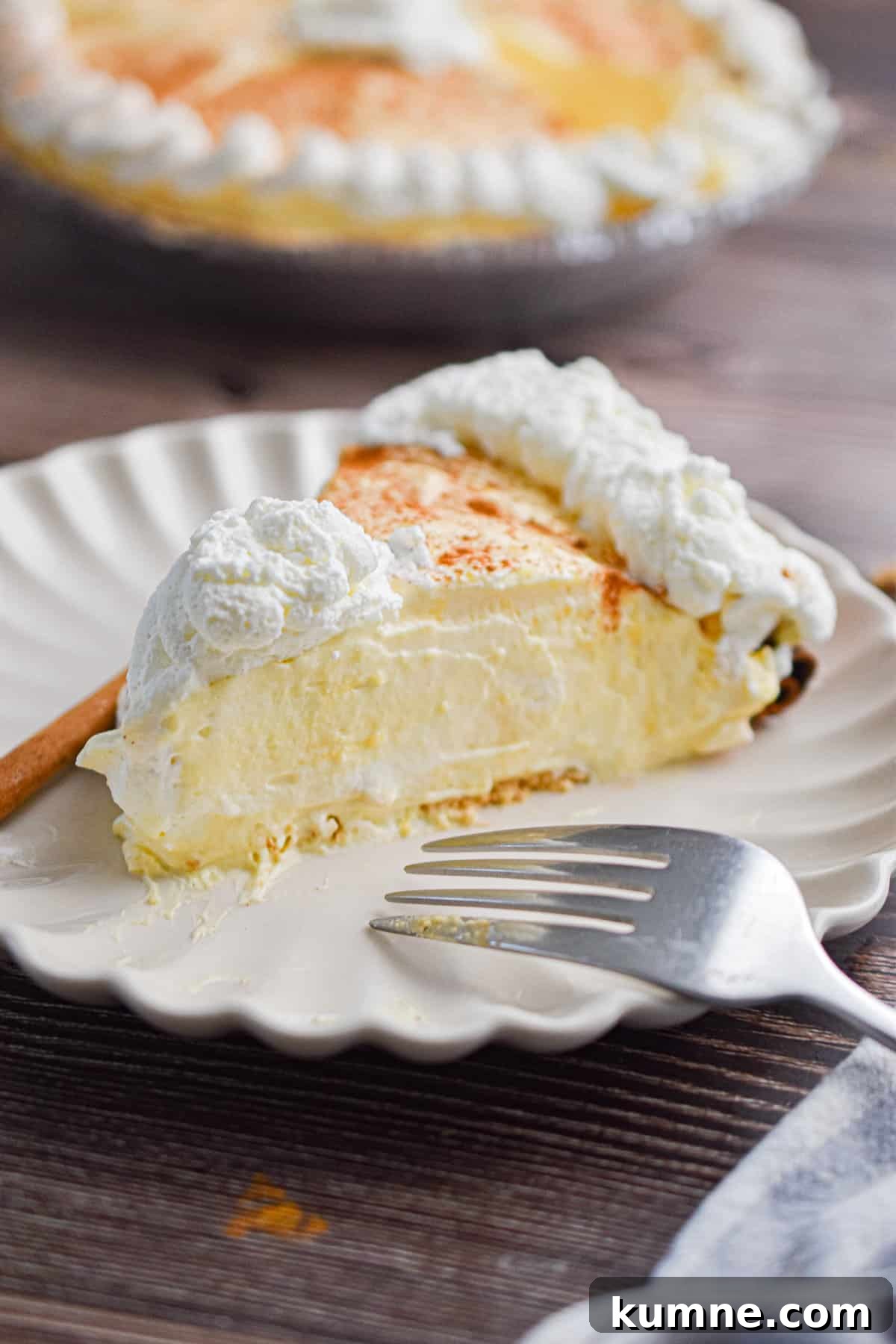 A slice of the no-bake eggnog pie is on a plate with a fork and a cinnamon stick.