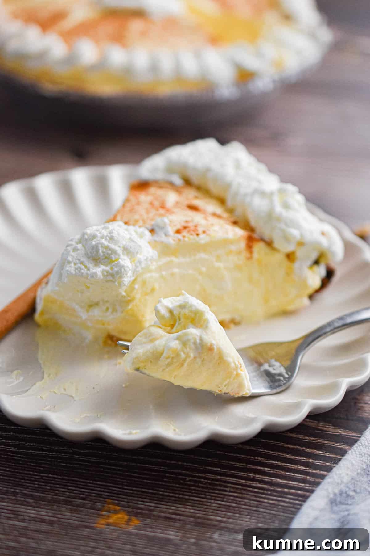 A piece of the no-bake eggnog pie is on a plate with a fork holding a piece of that pie.