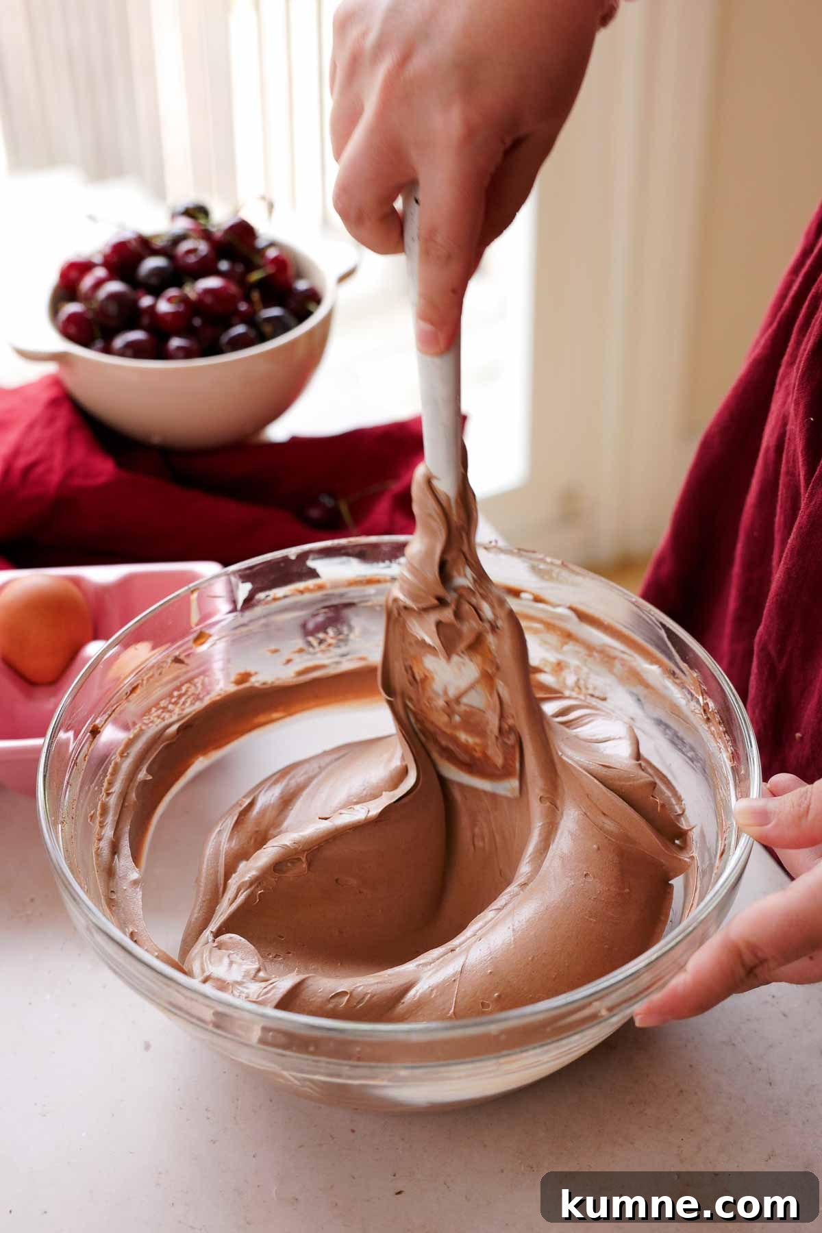 folding chocolate cheesecake batter with spatula in large glass bowl